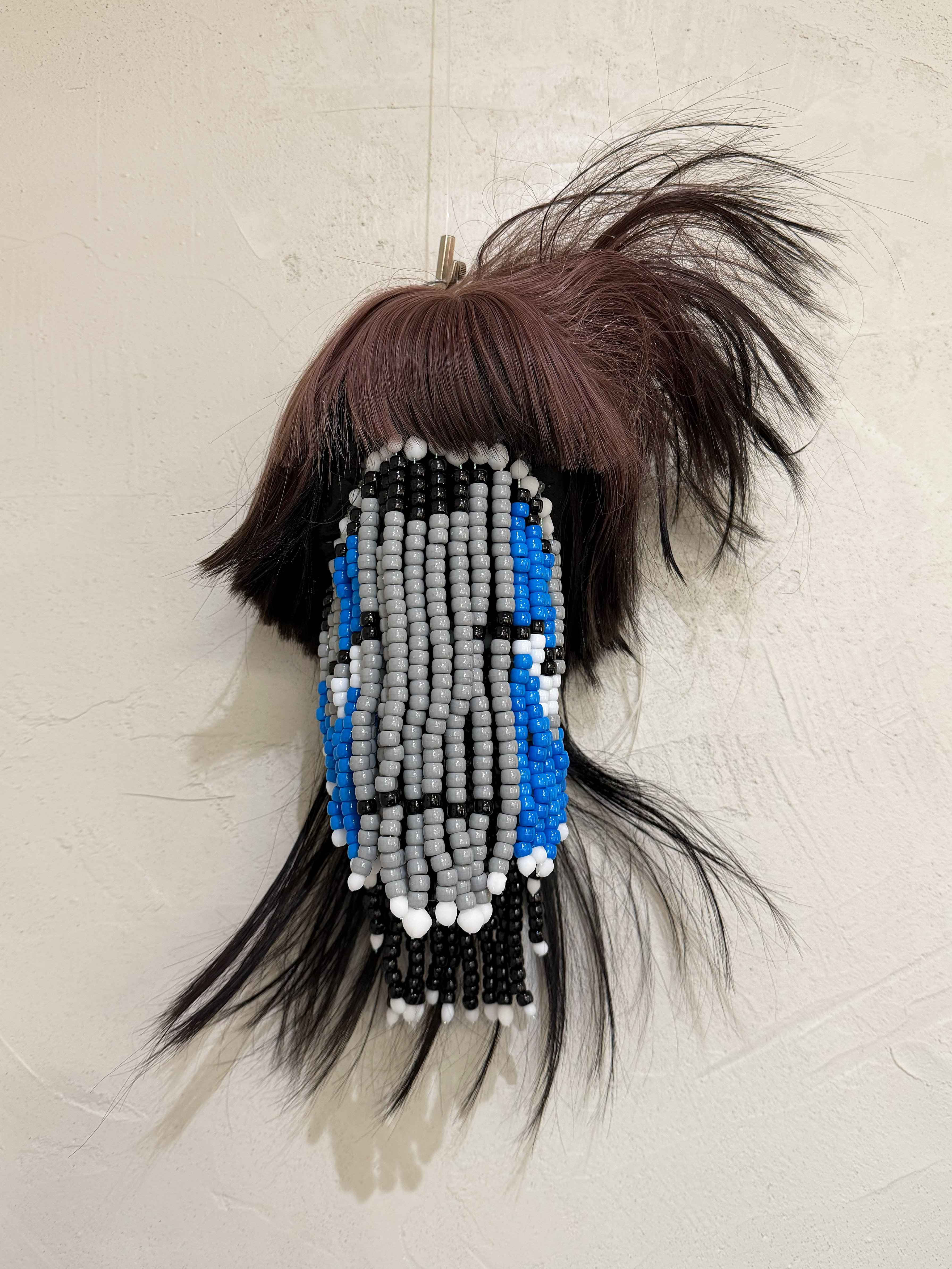 Frontal shot of a sculpture made using beads and a sythetic wig to represent a floating head.